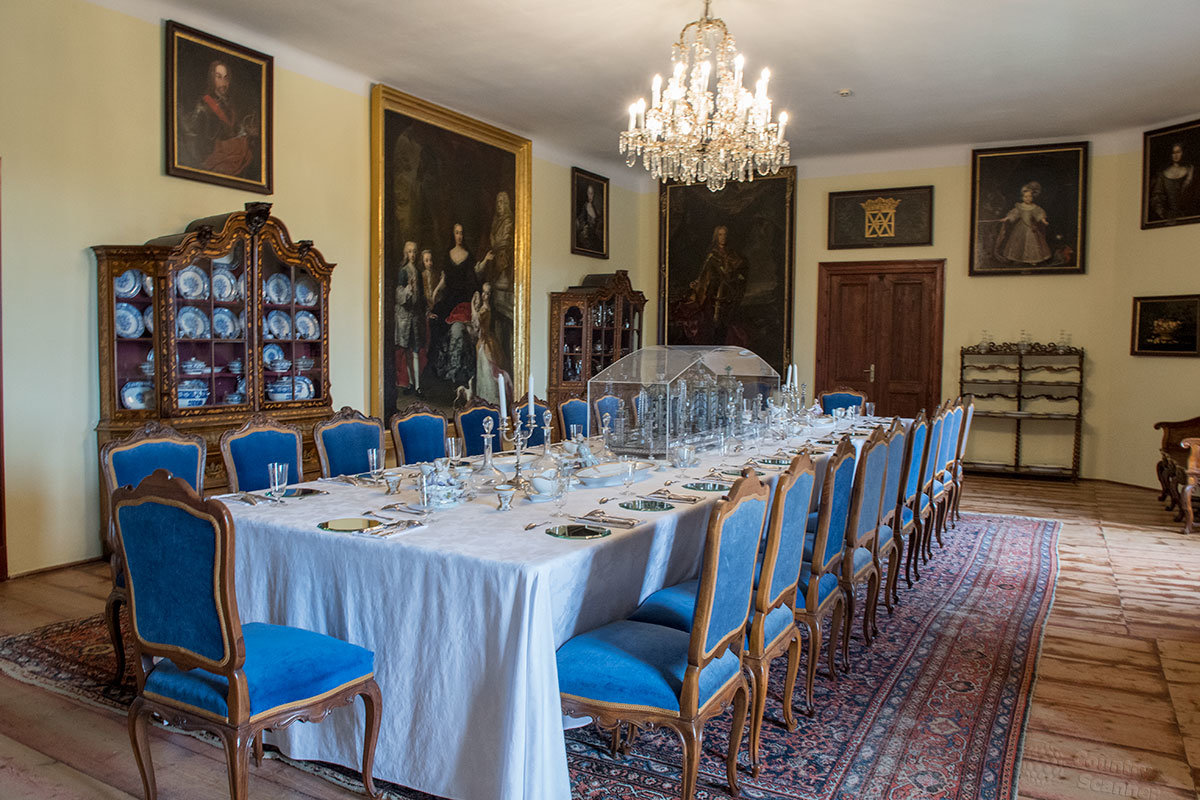 Парадная столовая замка Нелагозевес с сервированным обеденным столом на 22 персоны, живописные полотна и коллекционный фарфор в серванте.